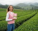 Woman holding a doze. ceremonial matcha pouch in a shade-grown green tea field with misty hills behind